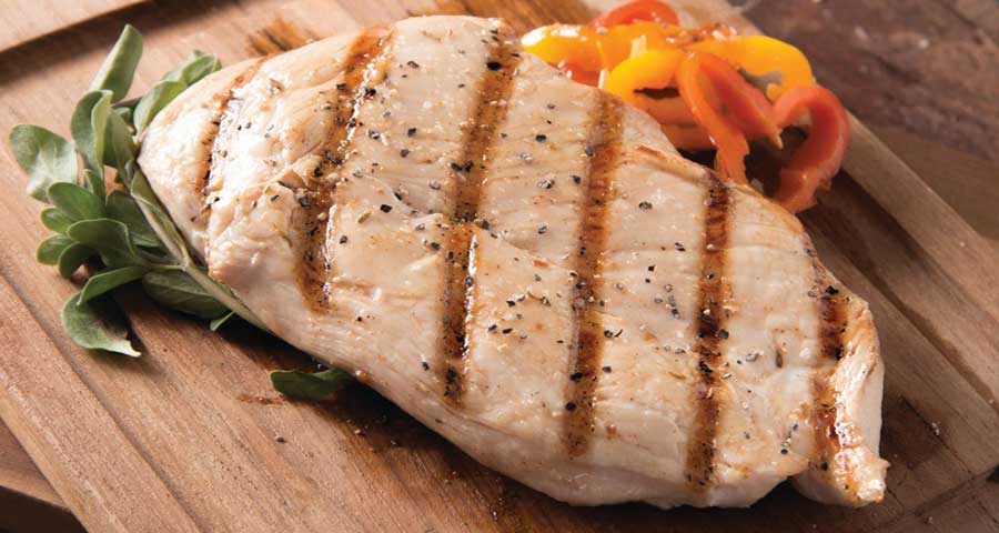 Grilled chicken and tomato on a wooden plate