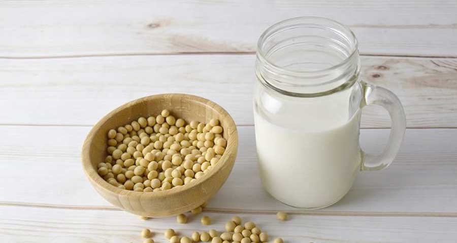 A glass of soya milk next to a bowl of soy beans